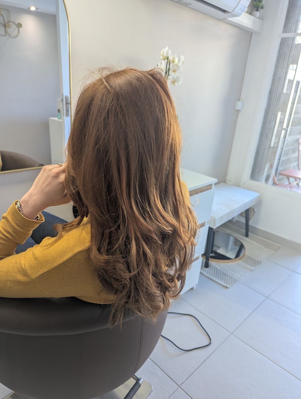 Un balayage châtain doré, coiffé en longueurs ondulées, photographié dans le salon.